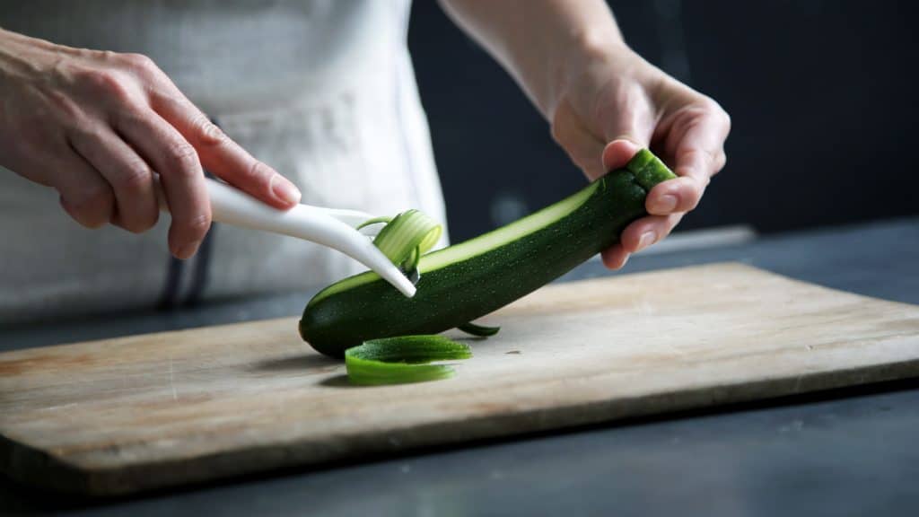 picture of a man demonstrating how to make courgette spaghetti using a peeler or cheese slicer to make long thin strips before chopping